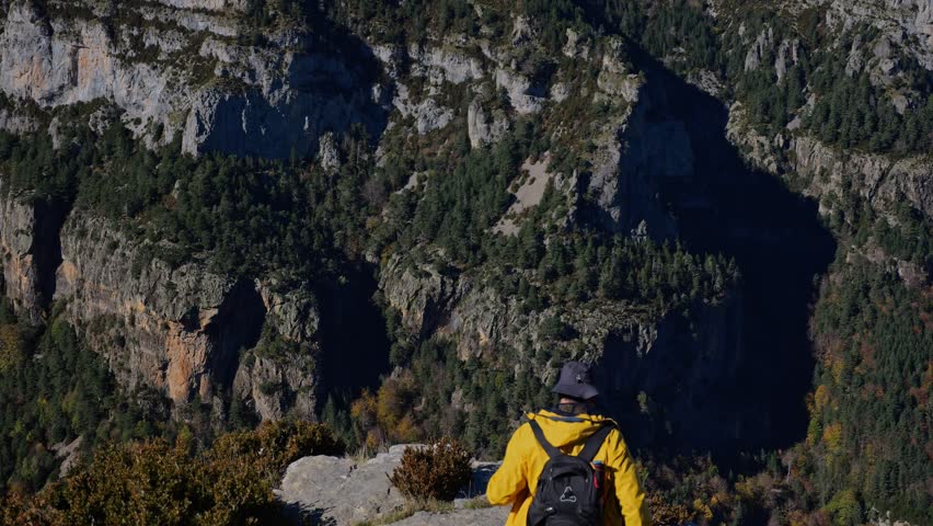 Male hiker reaches the place raising his hands up, holding trekking poles in his hands overlooking the beautiful mountain background. A traveler standing on a rock looking at an amazing highland.