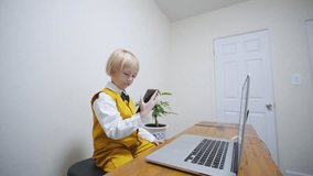 Zooming in portrait of cute caucasian boy watching something on the smartphone and smiling. 5 years old boy in bright waistcoat and trousers smiles at something on the phone