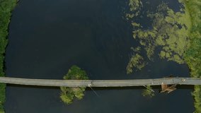 Aerial view vertically down of a suspension bridge with fishermen with fishing rods on steel ropes with a wooden deck over the Сhusovaya River in the forest. drone video