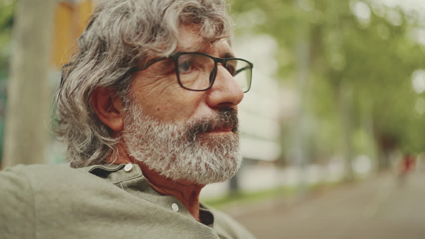 Clouse-up, smiling middle-aged man with gray hair and beard wearing casual clothes sits on bench. Mature gentleman in eyeglasses is resting on the bench | Shutterstock HD Video #1099000721