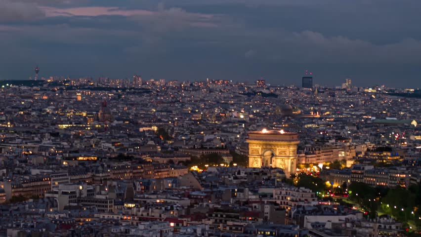 Cinematic establishing aerial panoramic view of Paris Arc de Triomphe illuminated Triumphal Arch, Paris Champs Elysees traffic circle street and Paris city streets at night