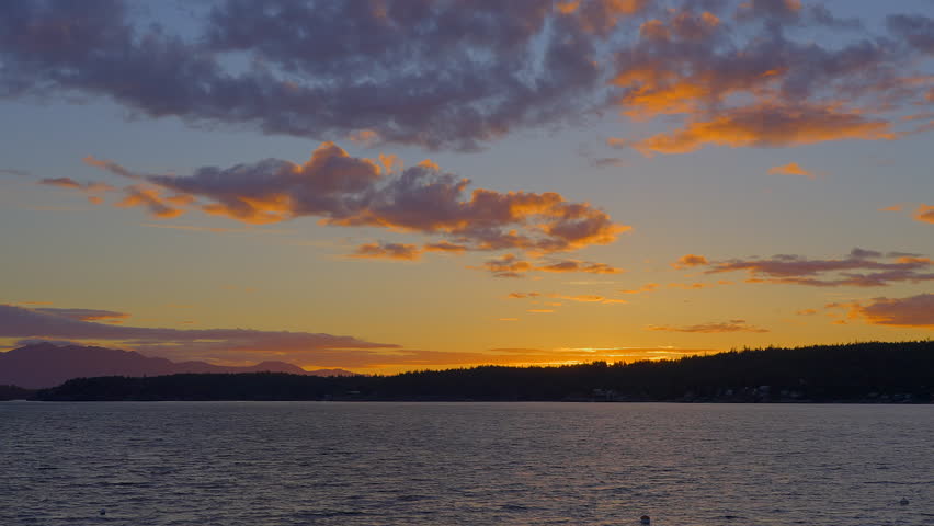 Establishing shot of ocean sunset over mountains in slow motion at summer day in Vancouver, Canada, North America. Evening time on September 2022. Still camera. ProRes 422 HQ.