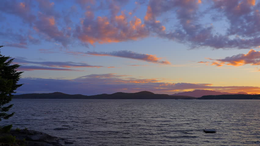 Establishing shot of ocean sunset over mountains in slow motion at summer day in Vancouver, Canada, North America. Evening time on September 2022. Still camera. ProRes 422 HQ.