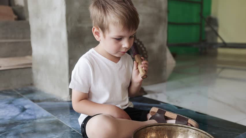 Boy playing singing bowls sitting on the floor