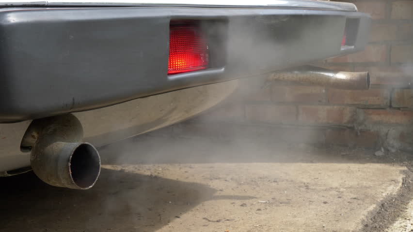Closeup of the rear end of a stationary old classic vintage car, just after being started, with fumes and moisture exiting the twin exhaust tailpipes. | Shutterstock HD Video #1099008395