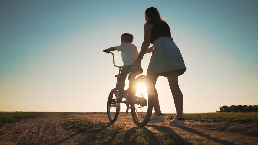 Happy family. Mom teaches her son to ride bike in park. My son is riding a bike for the first time. The child dreams of traveling by bike. The boy is learning to ride a bike. Mom helping hand to son. Royalty-Free Stock Footage #1099009033