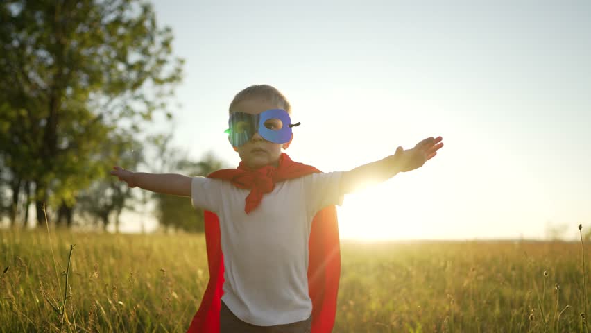 Boy in superhero costume. Child in red raincoat and mask runs through grass in park. Kid plays superhero in park at sunset. Child in suit runs through green grass at sunset. summer outdoor recreation | Shutterstock HD Video #1099009075