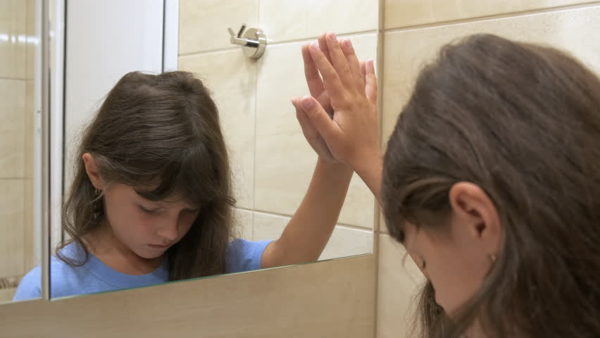 The child is sad at the mirror. A little girl looks sadly in the mirror.
