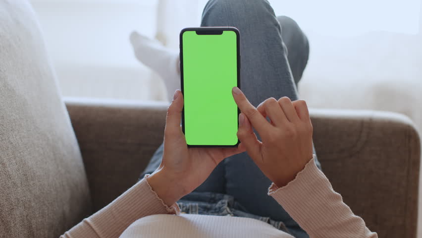 Close up shot of unrecognizable woman web surfing on smartphone with blank green chroma key screen, scrolling and tapping online, resting on sofa, slow motion, empty space for mockup | Shutterstock HD Video #1099017975