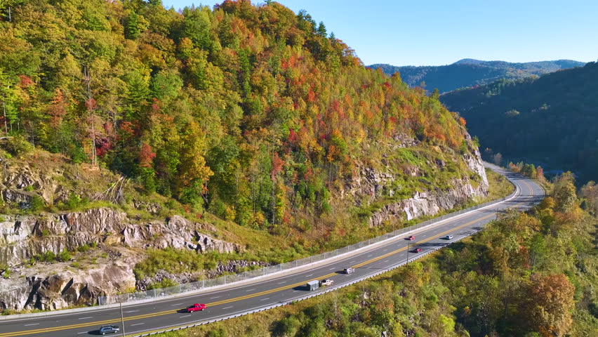 Aerial view of highway road in North Carolina through Appalachian mountains in golden fall season with fast moving trucks and cars. Interstate transportation concept