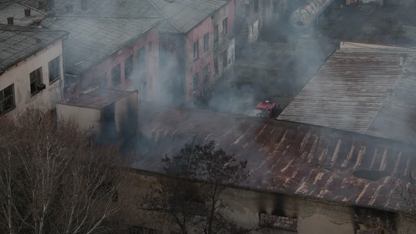 A large industrial factory building is burning down in city center. City district covered in dense clouds of smoke rising from building. Belgrade, Serbia 23.12.2022