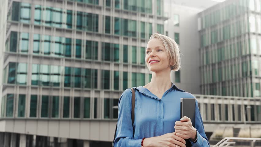 Confident business woman walking outdoors a modern office building. Portrait of young female corporate professional leaving the workplace after a successful day 