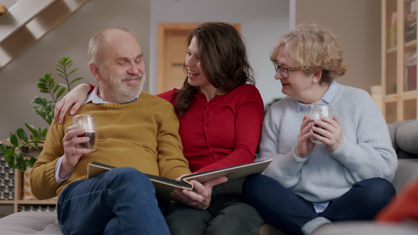 Young female sitting laughing with grandparents sharing memories looking through photo album | Shutterstock HD Video #1099024859