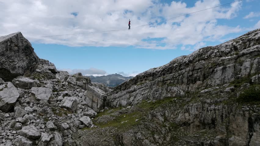Extreme sport of man jumping on slackline in mountains making tricks and having fun - aerial tilt up shot