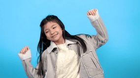 Asian schoolgirl dance in front of camera video with fun happiness, childhood lifestyle girl expression energy enjoy listening music smiling and jumping, cute little girl enjoy party blue background