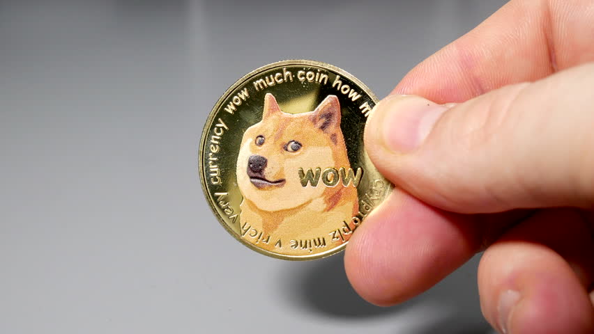 Gold dogecoin coin held between fingers in hand on gey table | Shutterstock HD Video #1099030791
