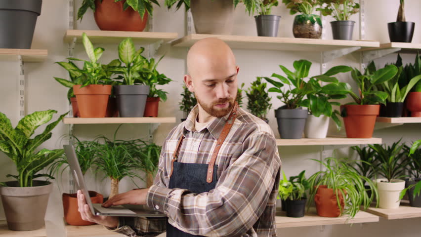 Caucasian entrepreneur man in the floral store using the laptop to checking the inventory of shop then looking to the camera smiling large