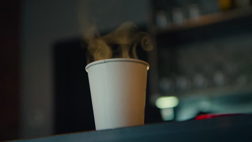 Customer pick up take away coffee order from cafe. Paper cup of take away hot beverage stand on top of table, steaming. Warm americano coffee in to go cup Royalty-Free Stock Footage #1099036295