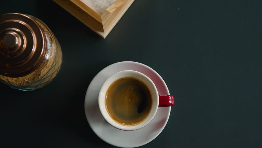 Person stir sugar in americano or espresso with small spoon. Top view on coffee cup on a table. Minimalistic clean shot of isolated coffee cup | Shutterstock HD Video #1099036299