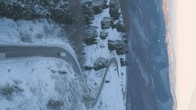 vertical video of drone follows delivery trucks through a mountain pass in a snowy setting