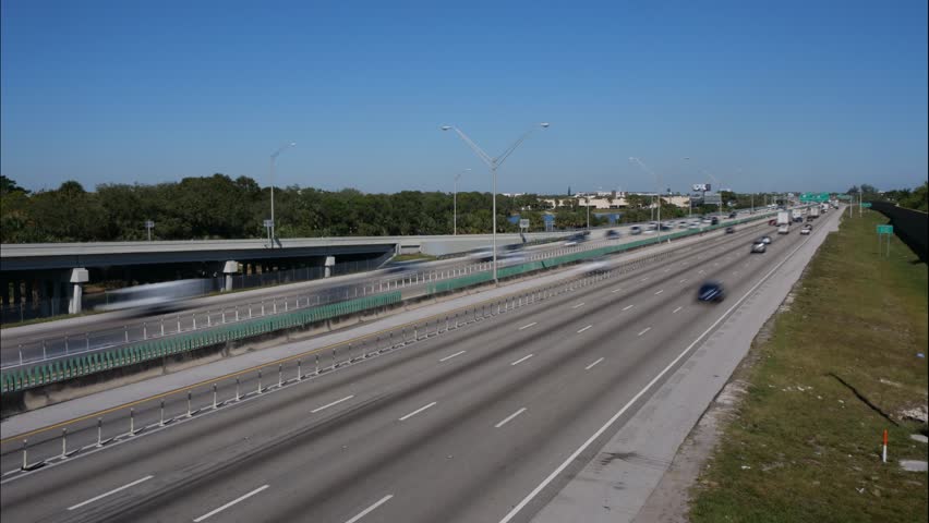 Traffic zips along I-95 southbound and northbound in Deerfield Beach, Florida at SW 10th Street from NE corner in a sunny day under clear blue sky.