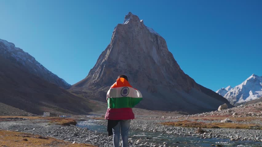 Wide angle shot of female Indian traveler holding Indian flag above her head in front of Gumbok Rangan mountain at Zanskar, Ladakh, India. Indian flag waving in the wind. Indian flag background