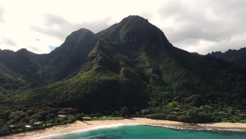 Cinematic Aerial view of island coast of Hawaii. Amazing white sand beach and tropical coral reef lagoon towards beautiful green mountains.Turquoise ocean water foaming. Tunnels beach, Kauai, Hawaii.