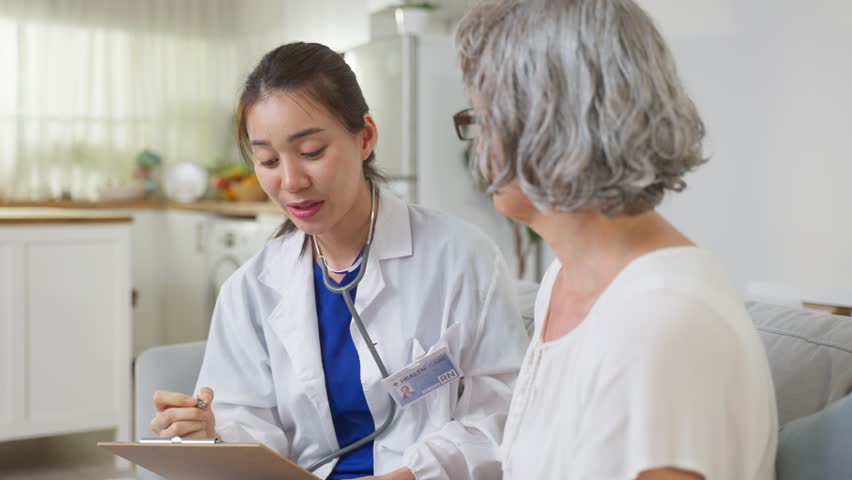 Asian caregiver nurse examine Caucasian senior woman patient at home. Attractive specialist carer women support, give advise and consult with older elderly mature grandmother in living room in house. | Shutterstock HD Video #1099040943