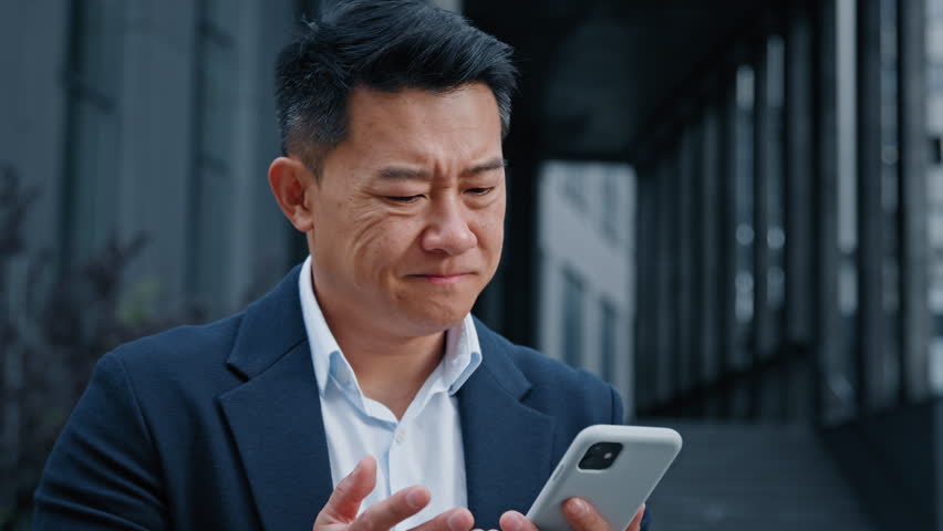Middle-aged Asian businessman in city 40s leader company CEO employer entrepreneur outdoors using phone sad upset with broken gadget online cellular problem bad connection lost failure with smartphone | Shutterstock HD Video #1099041849