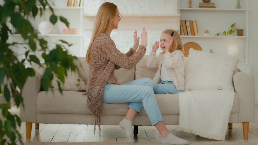 Cheerful Caucasian mother mum female babysitter and cute happy kid girl baby child daughter play patty cake clapping hands at home sitting on sofa having fun family enjoy funny game on couch together Royalty-Free Stock Footage #1099041863