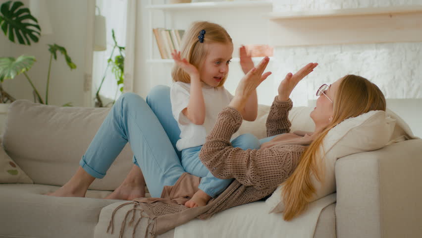 Happy parent Caucasian mom mother with cute kid daughter child girl baby playing patty cake game at home clapping hands lying on sofa couch at home living room carefree family having fun play together Royalty-Free Stock Footage #1099041885