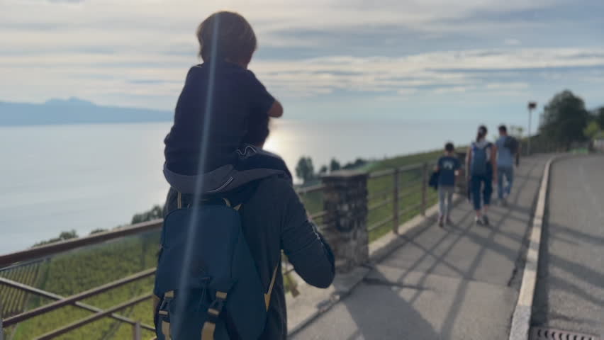 Back of little boy on mother shoulders walking outside in street traveling. Family on vacation