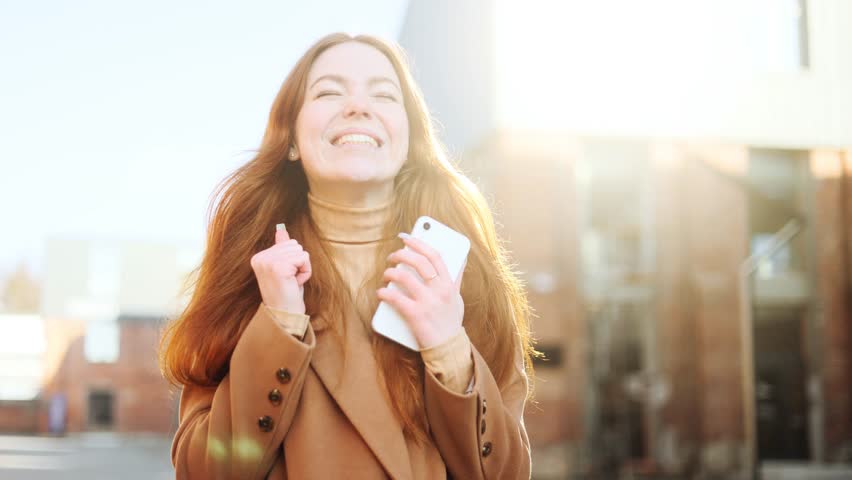 Overjoyed attractive young red haired ginger woman celebrate online win success reading great news message feel amazed happy Closeup of girl with good news on her phone screen | Shutterstock HD Video #1099046355