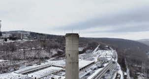 Winter aerial drone video with orbiting left movement of an old abandoned industrial concrete smokestack.