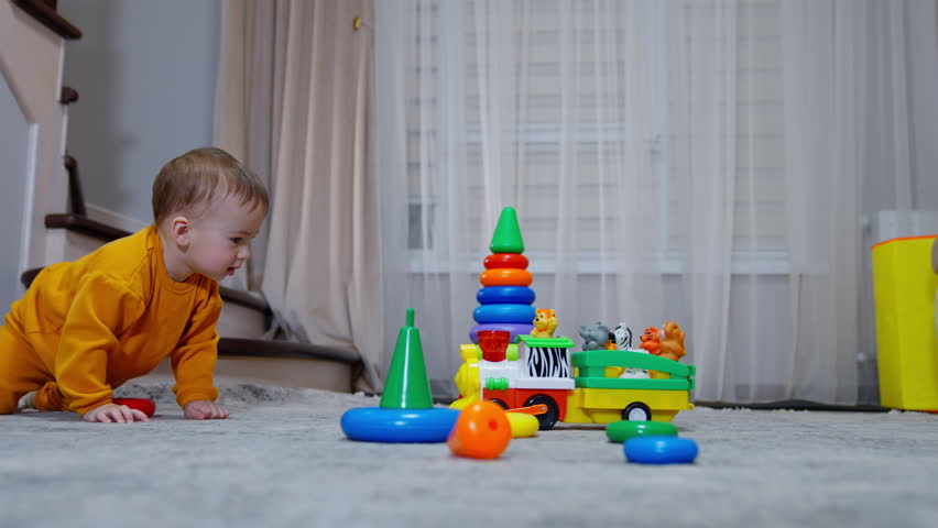 Happy cute active baby playing toys in the room. Kid looks at moving toy train and takes a ring from a pyramid to his mouth. Royalty-Free Stock Footage #1099047987