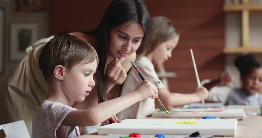 Close up cute focused little boy painting with gouache paint on canvas, young teacher artist woman helps, gives advices to preschooler art studio kid. Creativity, creative hobby and talent development Royalty-Free Stock Footage #1099050107