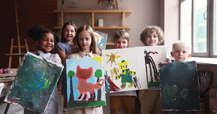Group of little multi ethnic kids showing their paintings painted during art class smile look at camera. Portrait of happy proud creative children pose together in workshop. Hobby, talent development Royalty-Free Stock Footage #1099050113