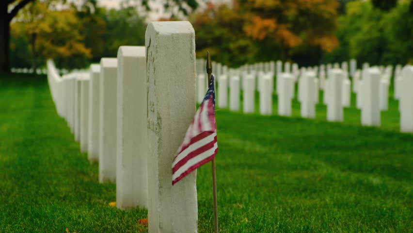 Second World War Cemetery. Military Cemetery Decorated for Memorial Day. American flag with stripes and stars flutters in strong wind. Cemetery graveyard white tombstones at sunset sky  Royalty-Free Stock Footage #1099050485