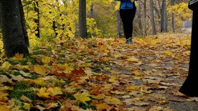 Woman running with Slim female legs and feet close up on autumn morning. Two women walking past. Young fitness sport woman running on autumn road. Slow motion of Young women exercising healthy concept