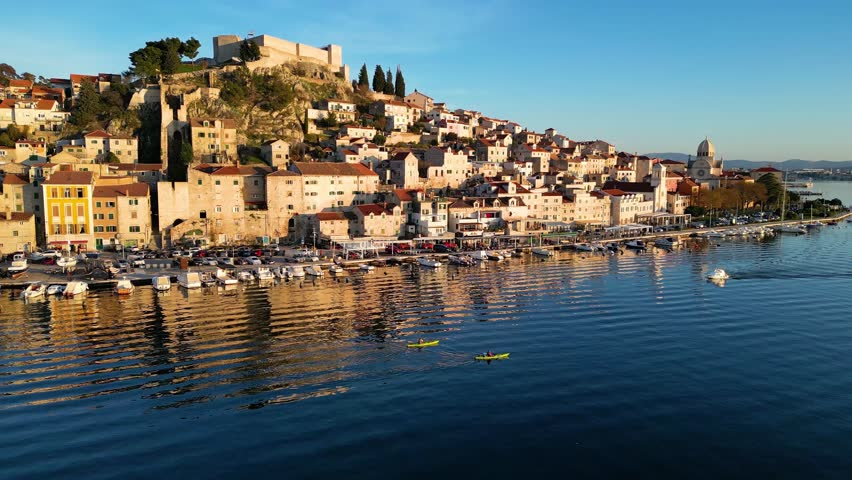 Aerial drone view of Sibenik town in Croatia during beautiful sunset colors, with a boat passing on the sea. Vacations and holidays on the seacoast. The Cathedral of St James in Sibenik Unesco.