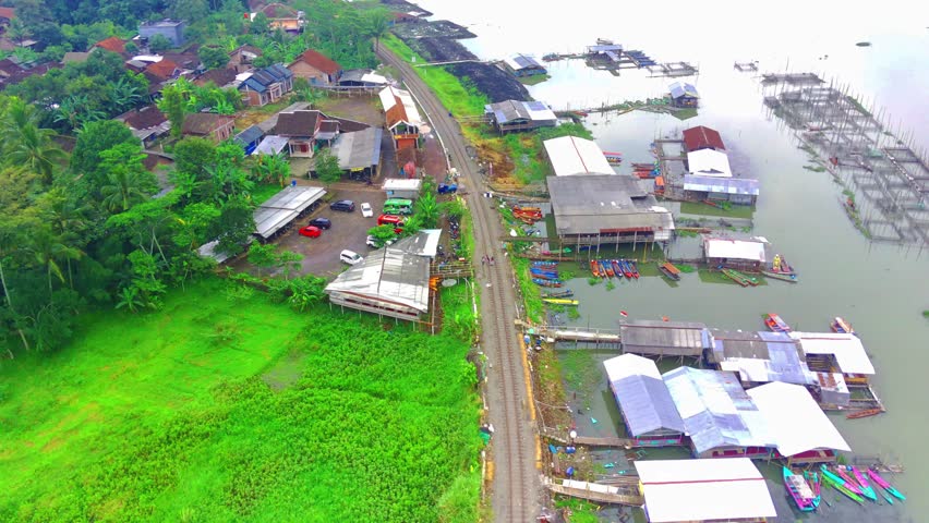 Flying over the Rawapening lake with boats and floating restaurants near the railways. Aerial shot.