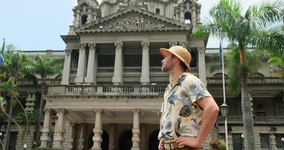 Smiling Hipster man in Glasses with Bag Walking, Looking around at Old City Street. Student, Tourist Concept. Traveling. a man in a safari hat stands near an architectural building in the city center