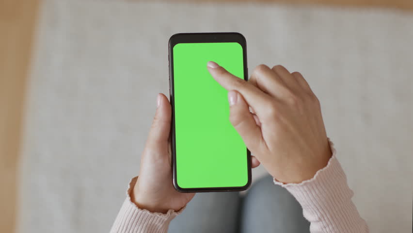 Mobile app ad. Close up shot of unrecognizable woman using smartphone with green chroma key screen, scrolling and tapping on device, top view, slow motion, empty space | Shutterstock HD Video #1099055503