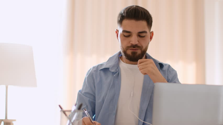 Convenient work. Young positive arab guy working on laptop and listening music online via earphones, working on laptop at home office, tracking shot, slow motion, empty space | Shutterstock HD Video #1099055513