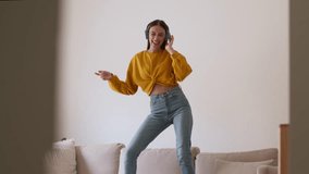 Carefree domestic pastime. Young happy slim woman wearing headphones listening to music and dancing on sofa, fooling around at home, slow motion, free space - Powered by Shutterstock - Get 15% off with code: PIKWIZARD15