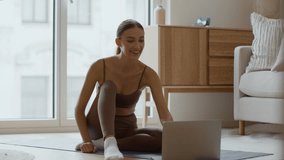 Online meditation concept. Young happy woman sitting in lotus position and start meditating, watching video lesson on laptop, tracking shot, slow motion, empty space