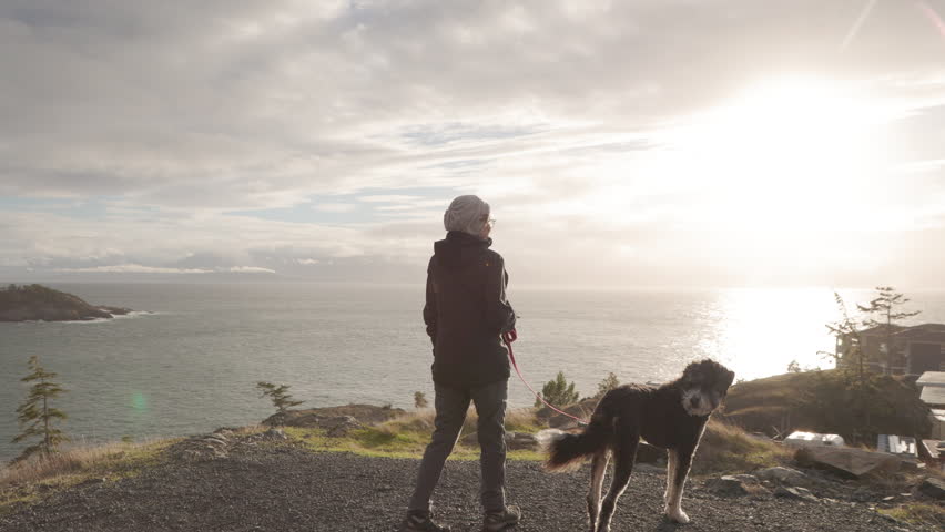 Older woman walking her dog by the ocean, sunny day, seaside, retirement life, pet ownership, good dog. 4K PRORES 422 24FPS