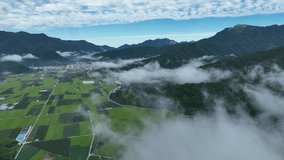 A drone video of a village seen through white clouds rising over a mountain viewed from above