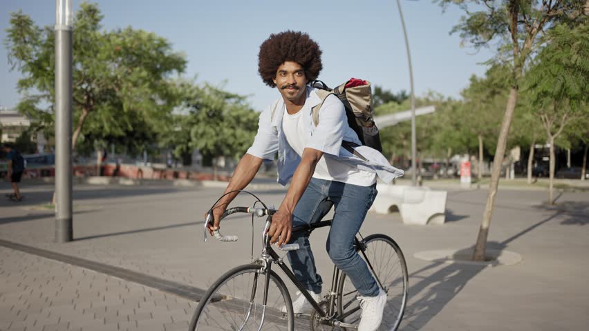 Young African American hipster man with bag riding bicycle on city street going to work  | Shutterstock HD Video #1099062897