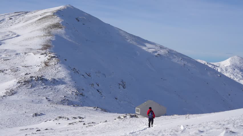 A hiker walks in the snow towards the mountain bivouac shelter